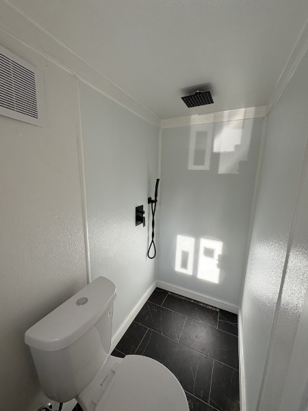 Walk-in shower with a rain shower head and matte-black fixtures over dark tile