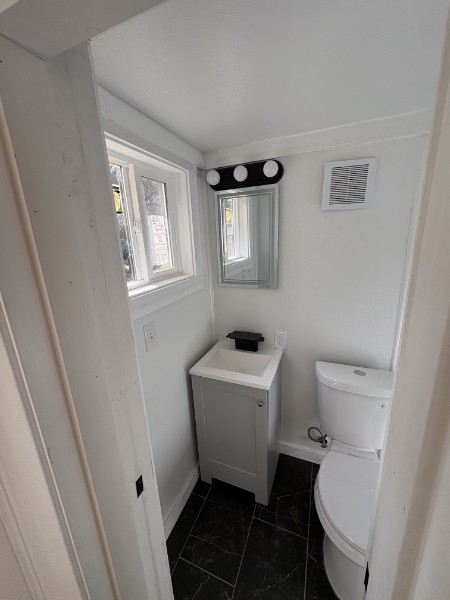 Compact full bathroom with a white vanity, framed mirror, and marble-look tile floor